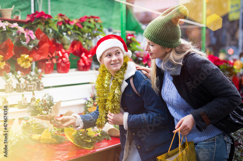 Teenage girl and her mother purchasing christmas bouquet at market outdoors.