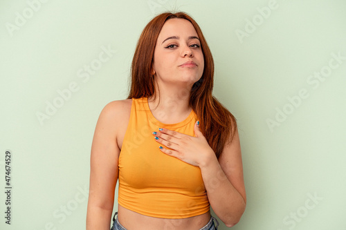 Young caucasian woman isolated on green background taking an oath, putting hand on chest.