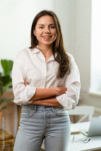 Image of young cheery positive beautiful business woman sitting indoors in office or home office using laptop computer. © arthurhidden