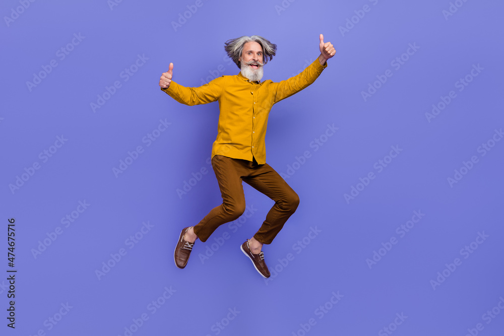 Full length body size view of attractive cheery gray-haired man jumping showing thumbup isolated over bright violet purple color background