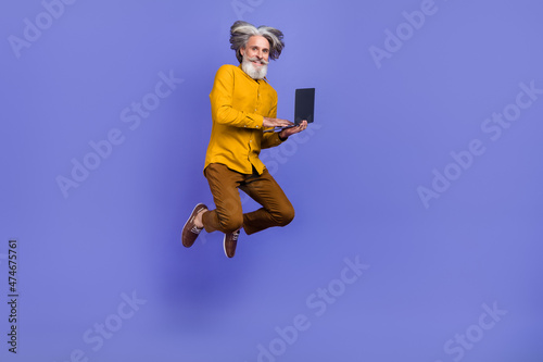 Full length body size view of bearded trendy cheery gray-haired man jumping using laptop isolated over bright violet purple color background