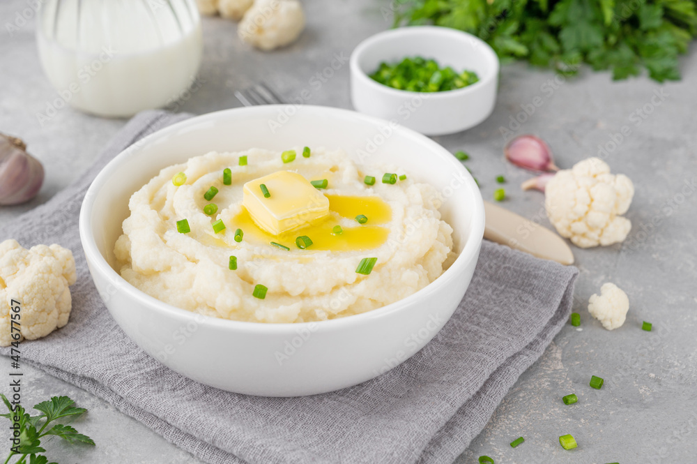 Cauliflower puree with butter and green onions in a white bowl on a gray concrete background. Healthy food. Copy space. Cauliflower puree with butter and green onions in a white bowl on a gray concrete background. Healthy food. Copy space.