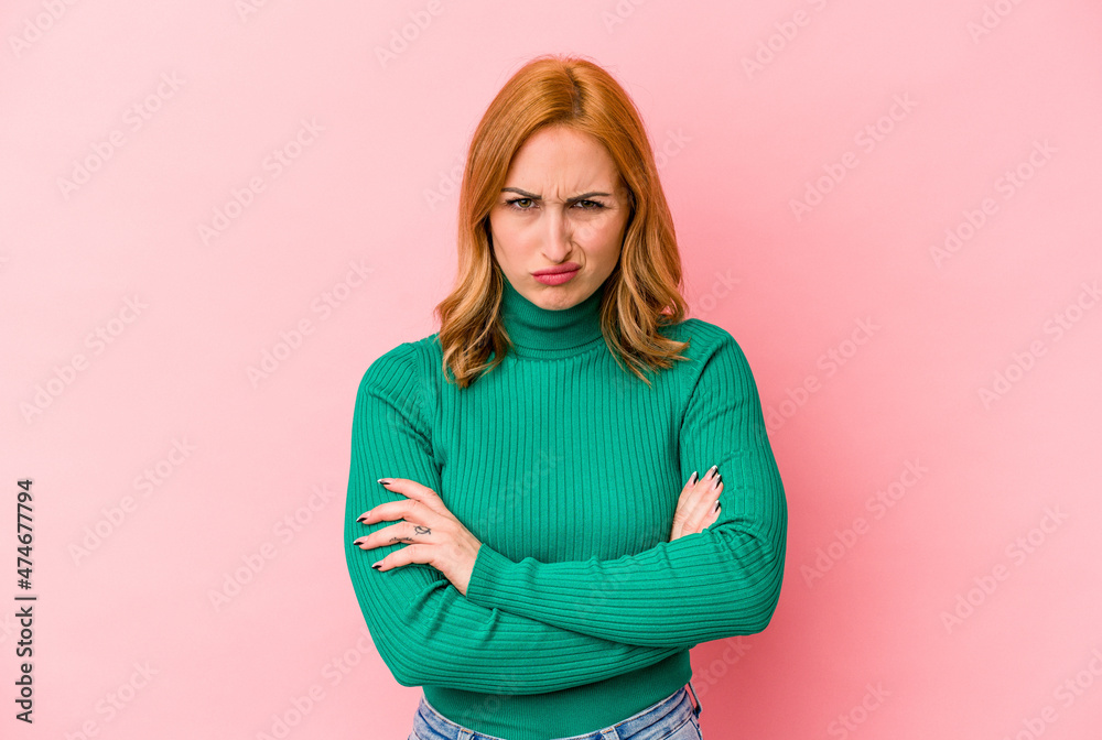Young caucasian woman isolated on pink background frowning face in displeasure, keeps arms folded. Young caucasian woman isolated on pink background frowning face in displeasure, keeps arms folded.