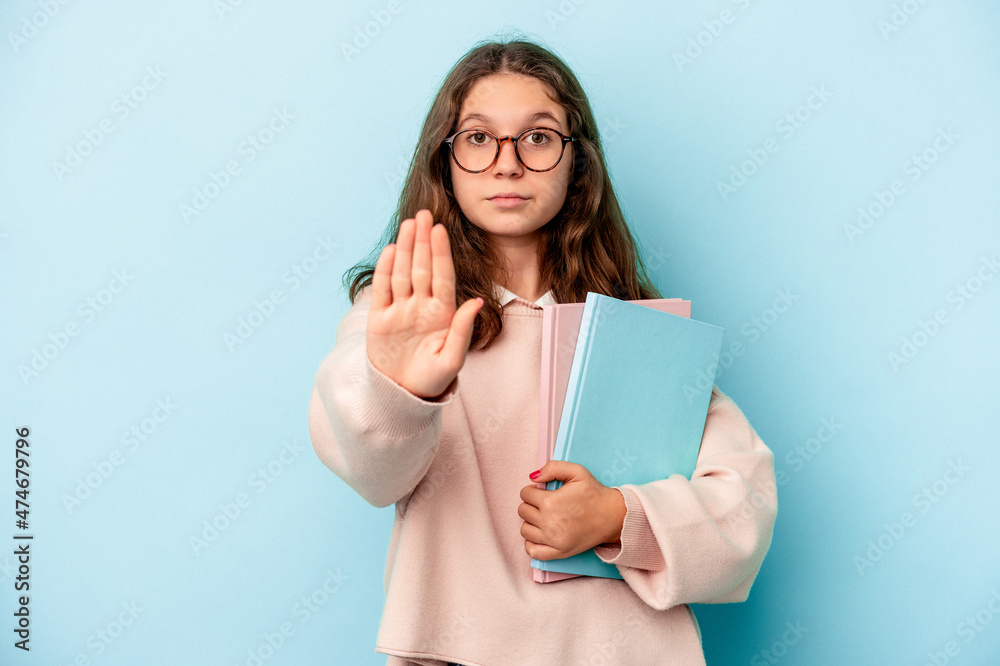 Little caucasian student girl holding books isolated on blue background standing with outstretched hand showing stop sign, preventing you. Little caucasian student girl holding books isolated on blue background standing with outstretched hand showing stop sign, preventing you.