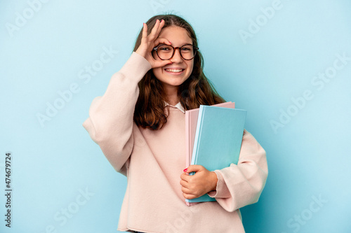 Little caucasian student girl holding books isolated on blue background excited keeping ok gesture on eye.