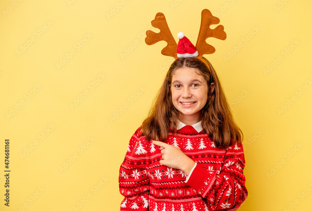 Little caucasian girl wearing a Christmas reindeer hat isolated on yellow background smiling and pointing aside, showing something at blank space. Little caucasian girl wearing a Christmas reindeer hat isolated on yellow background smiling and pointing aside, showing something at blank space.