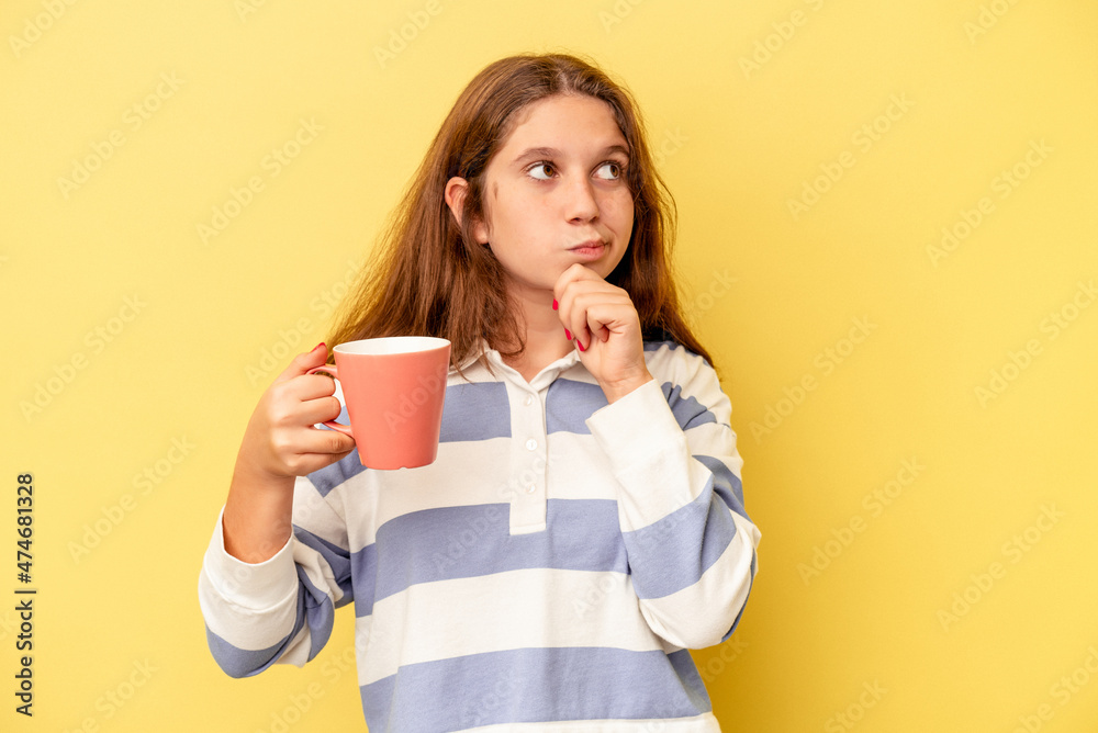 Little caucasian girl holding a pink mug isolated on yellow background looking sideways with doubtful and skeptical expression. Little caucasian girl holding a pink mug isolated on yellow background looking sideways with doubtful and skeptical expression.