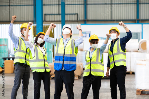 Multicultural engineering worker team celebrate a great success in warehouse. People wearing protective face mask prevent covid-19 virus