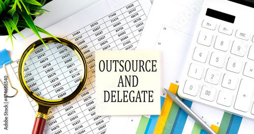 OUTSOURSE AND DELEGATE text on sticker on diagram with magnifier and calculator. Business concept