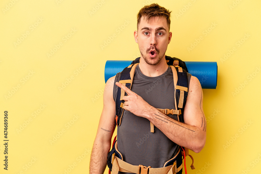 Young hiker caucasian man isolated on yellow background pointing to the side Young hiker caucasian man isolated on yellow background pointing to the side