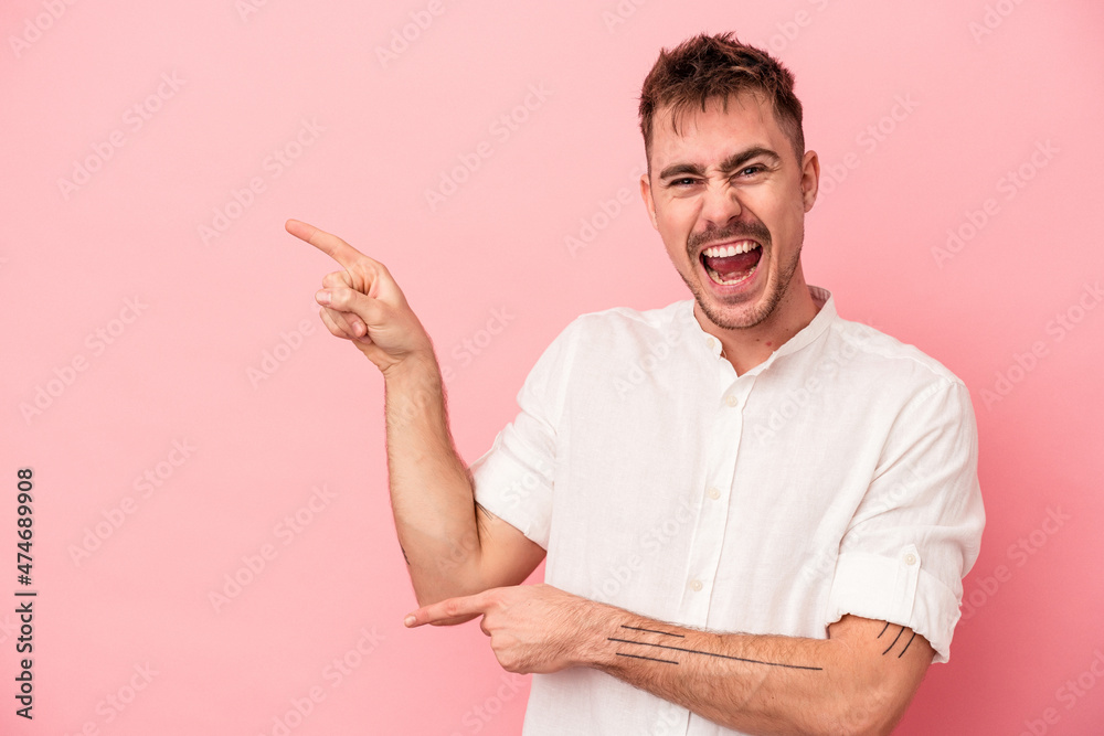 Young caucasian man isolated on pink background pointing with forefingers to a copy space, expressing excitement and desire.