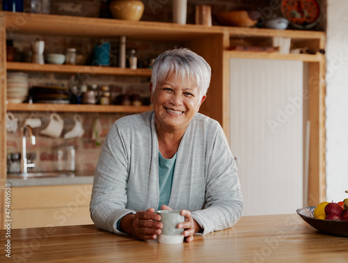 Portrait of retired biracial elderly female leaning on kitchen counter smiling at camera.