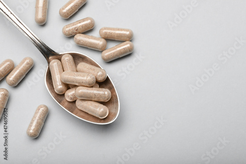 Many gelatin capsules and spoon on light grey background, flat lay. Space for text