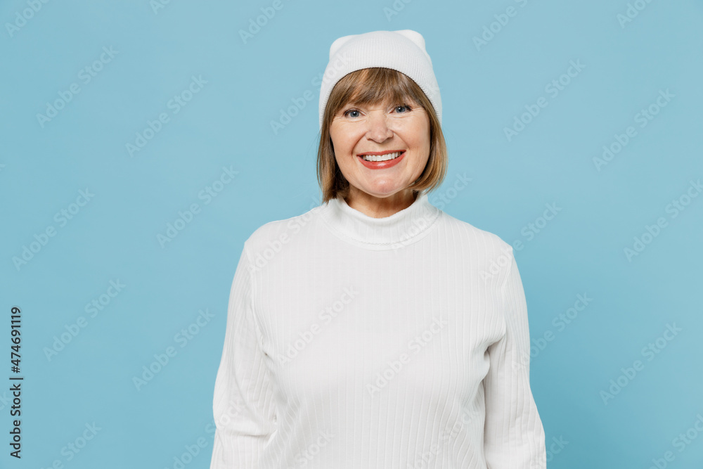 Elderly smiling cheerful happy fun satisfied grandmother caucasian woman 50s in white knitted sweater hat look camera isolated on plain blue color background studio portrait. People lifestyle concept. Elderly smiling cheerful happy fun satisfied grandmother caucasian woman 50s in white knitted sweater hat look camera isolated on plain blue color background studio portrait. People lifestyle concept.