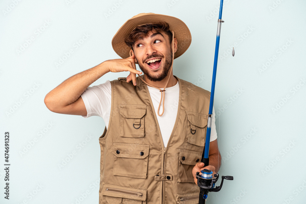 Young mixed race fisherman holding a rod isolated on blue background showing a mobile phone call gesture with fingers. Young mixed race fisherman holding a rod isolated on blue background showing a mobile phone call gesture with fingers.