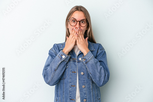 Young caucasian woman isolated on blue background shocked covering mouth with hands.