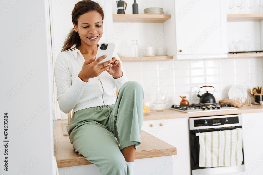 Young black woman smiling while using cellphone in kitchen Young black woman smiling while using cellphone in kitchen