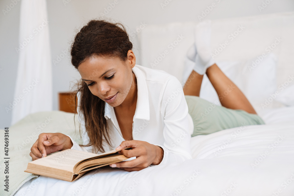 Young black woman reading book while lying on bed Young black woman reading book while lying on bed