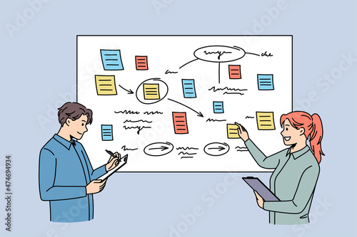 Discussion and business partners concept. Young smiling colleagues woman and man standing at presentation with notes discussing ideas together 