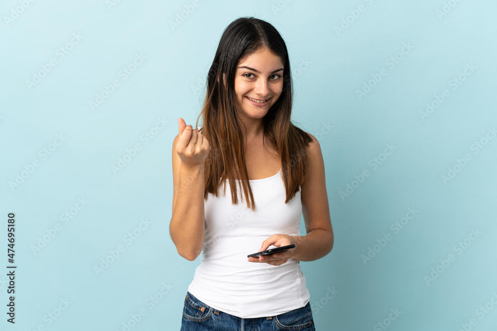 Young caucasian woman using mobile phone isolated on blue background making money gesture Young caucasian woman using mobile phone isolated on blue background making money gesture