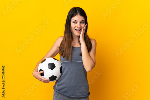Young football player woman isolated on yellow background with surprise and shocked facial expression © luismolinero