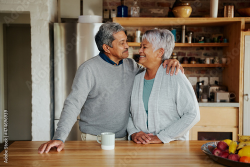 Happily retired elderly biracial couple smiling at each other lovingly in modern kitchen. Hugging, living healthy lifestyle in modern kitchen.