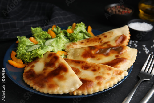 Delicious fried chebureki with vegetables served on black table