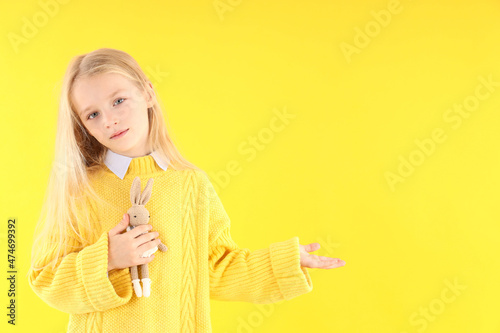 Cute little girl holds toy rabbit on yellow background