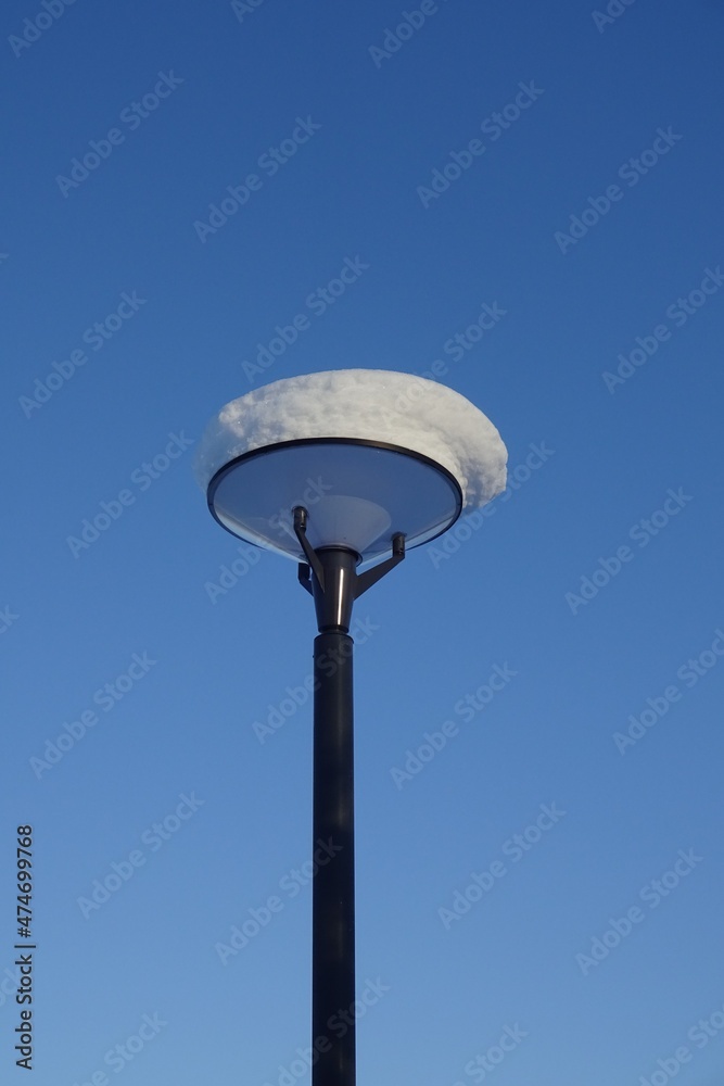 One ssolated street lamp with thick layer of snow on the top against blue clear sky. Winter season, close up view. Reidi tee street, Tallinn, Estonia. December 2021 One ssolated street lamp with thick layer of snow on the top against blue clear sky. Winter season, close up view. Reidi tee street, Tallinn, Estonia. December 2021