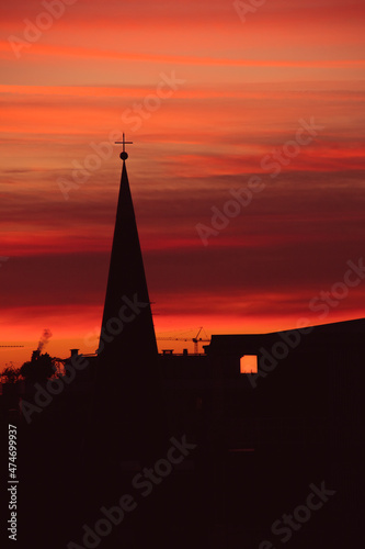 Urban winter sunset silhouette of the roofs of an italian city. Streaked burning red and orange sky, church steeple, see through lit windows. Cozy atmosphere, magic scenery. Golden hour.
