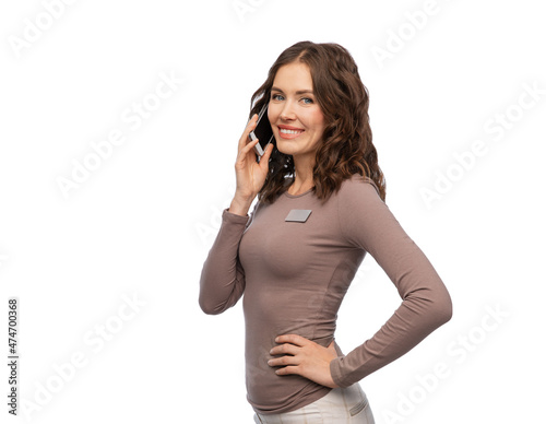sale, shopping and business concept - happy female shop assistant with name tag calling on smartphone over white background