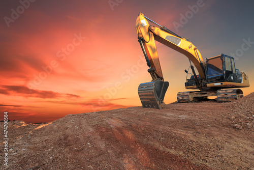 Yellow  Excavators are digging the soil in the construction site on the  orange  sky background