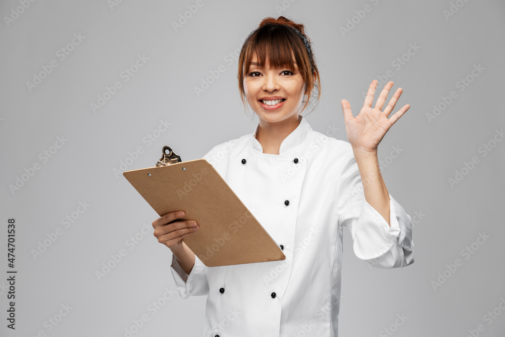 cooking, culinary and people concept - happy smiling female chef with clipboard waving hand over grey background cooking, culinary and people concept - happy smiling female chef with clipboard waving hand over grey background