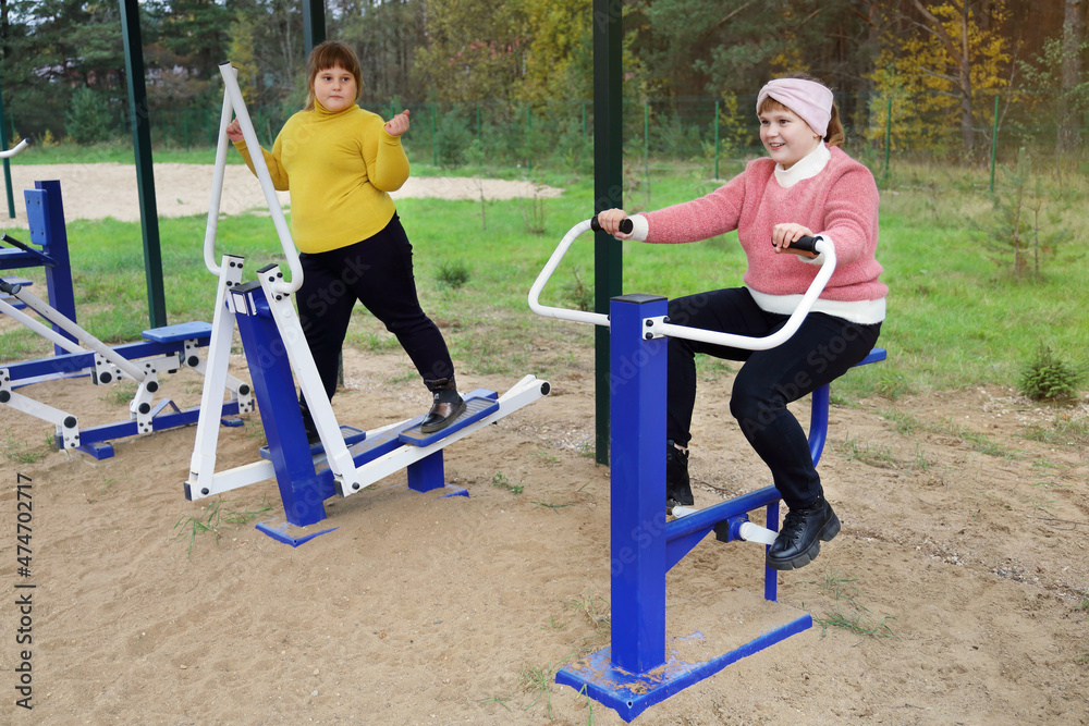 Two chubby girls performs sports exercises on street simulators, motivation to healthy lifestyle Two chubby girls performs sports exercises on street simulators, motivation to healthy lifestyle