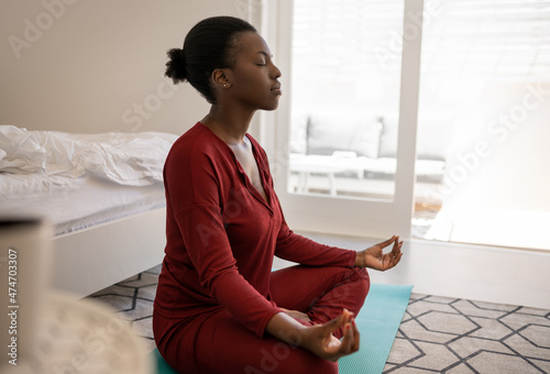 Black African woman meditating on yoga mat in bedroom, lotus pose