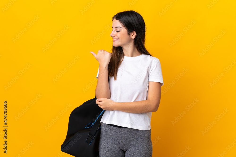 Young sport woman with sport bag isolated on yellow background pointing to the side to present a product Young sport woman with sport bag isolated on yellow background pointing to the side to present a product