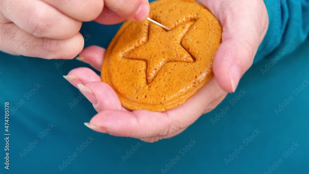 closeup female hand scratches with needle yellow caramel sugar cookies with embossed star for popular Korean children's game, cut out figure with needle, do not crumble pattern, holiday homemade food closeup female hand scratches with needle yellow caramel sugar cookies with embossed star for popular Korean children's game, cut out figure with needle, do not crumble pattern, holiday homemade food