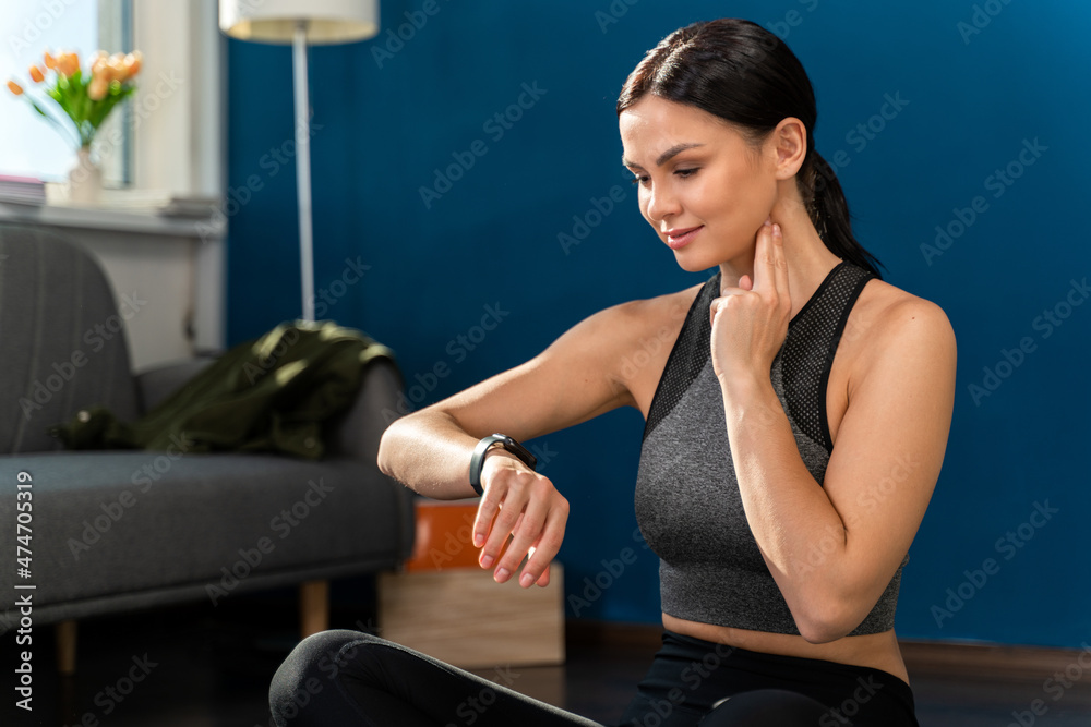 Obraz premium Fit woman looking at smartwatch and counting calories burned. Woman relaxed after workout and checking heart rate with smartwatch