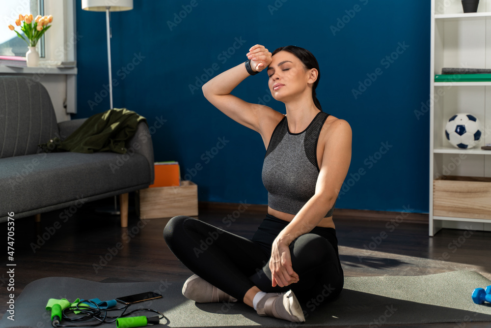 Break after training. Tired woman sitting on mat at home in the room while doing sports. Good morning after warm up. Fitness concept Break after training. Tired woman sitting on mat at home in the room while doing sports. Good morning after warm up. Fitness concept