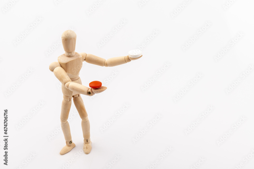 A wooden Gestalta doll or mannequin holds red and white pills in its hands on light background. The concept of choice. A wooden Gestalta doll or mannequin holds red and white pills in its hands on light background. The concept of choice.