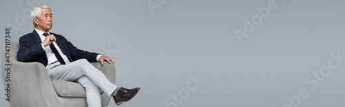 Foto elderly asian businessman in formal wear sitting in armchair isolated on grey, b