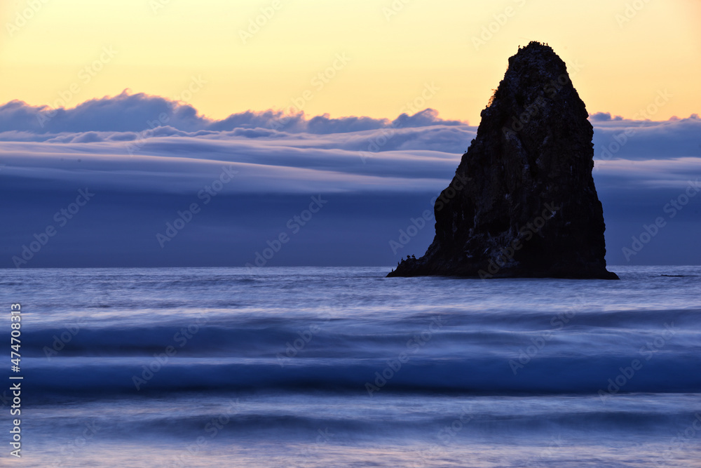 Islands of rock arise from the water and waves of the shoreline of Cannon Beach, Oregon during the grey evening twilight.