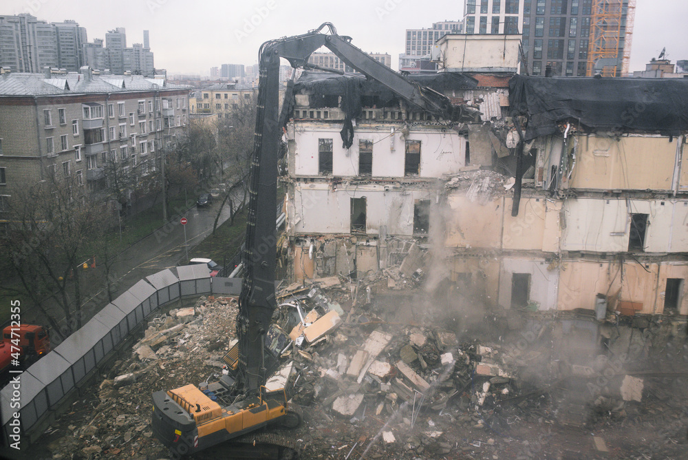 Construction equipment destroys a house on the site. Dismantling and demolition of a building in the city. The wreckage of an old abandoned house. Clearing land for the construction of a new building