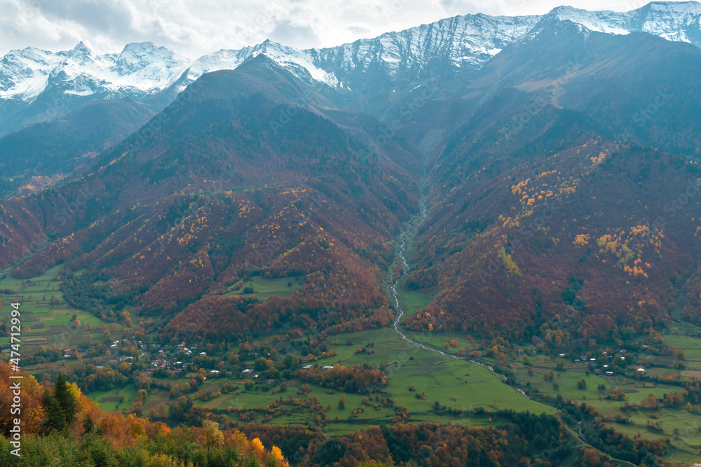 Obraz premium Small village at the foot of the greatest Caucasus mountains on an autumn day. Beautiful landscape of autumn mountains