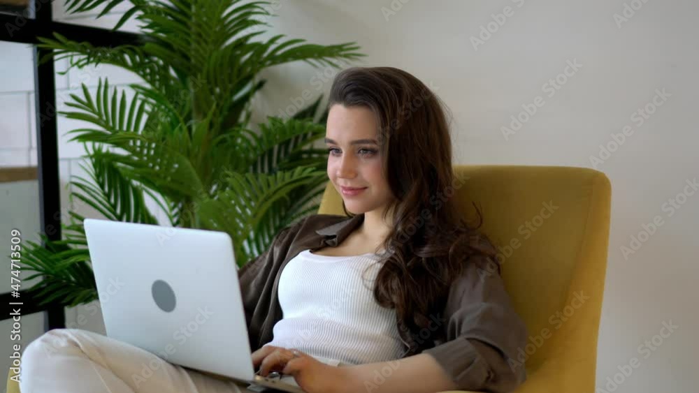 Brunette hair female smiling freelancer typing text on keyboard of laptop computer while working remote in modern home interior. 25 years old positive young woman enjoying studying online via netbook Brunette hair female smiling freelancer typing text on keyboard of laptop computer while working remote in modern home interior. 25 years old positive young woman enjoying studying online via netbook