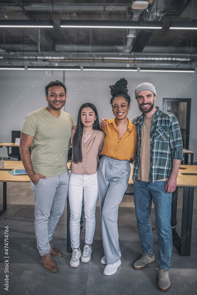 Obraz premium Four interracial young people standing hugging at office