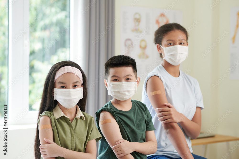 Group of children in medical masks having adhesive plasters on arms after getting vaccine against covid-19