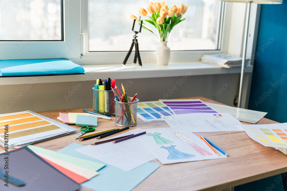 Paints, colored pencils, and sketches of unusual creative dresses laying at the table. Workplace of a women's costume designer concept Paints, colored pencils, and sketches of unusual creative dresses laying at the table. Workplace of a women's costume designer concept
