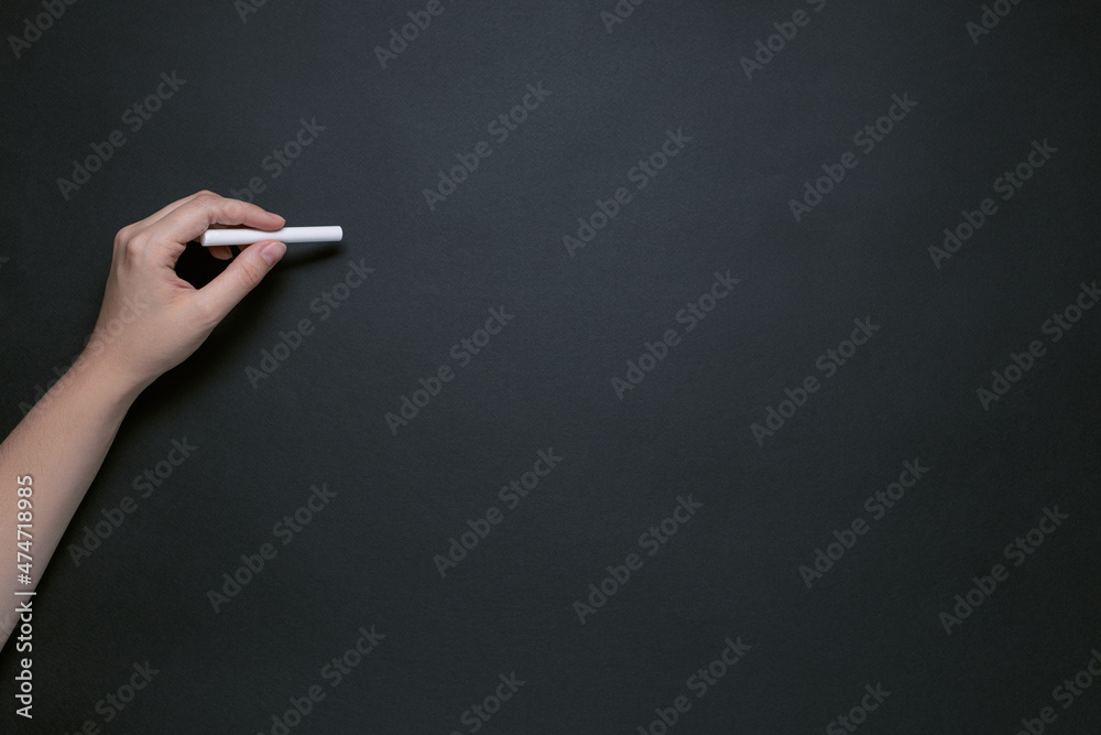 Naklejka premium hand with chalk on black chalkboard, place for text, basis for design, left-handed concept