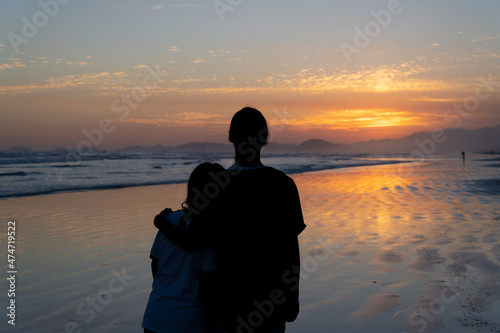 Dois garotos amigos observando o por do sol na praia. Silhueta de duas pessoas